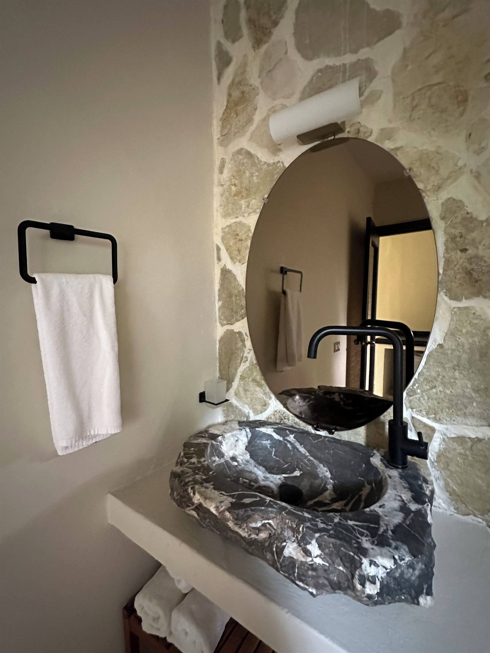 El Rincón de Abi: bathroom with a stone wall, marble sink and round mirror